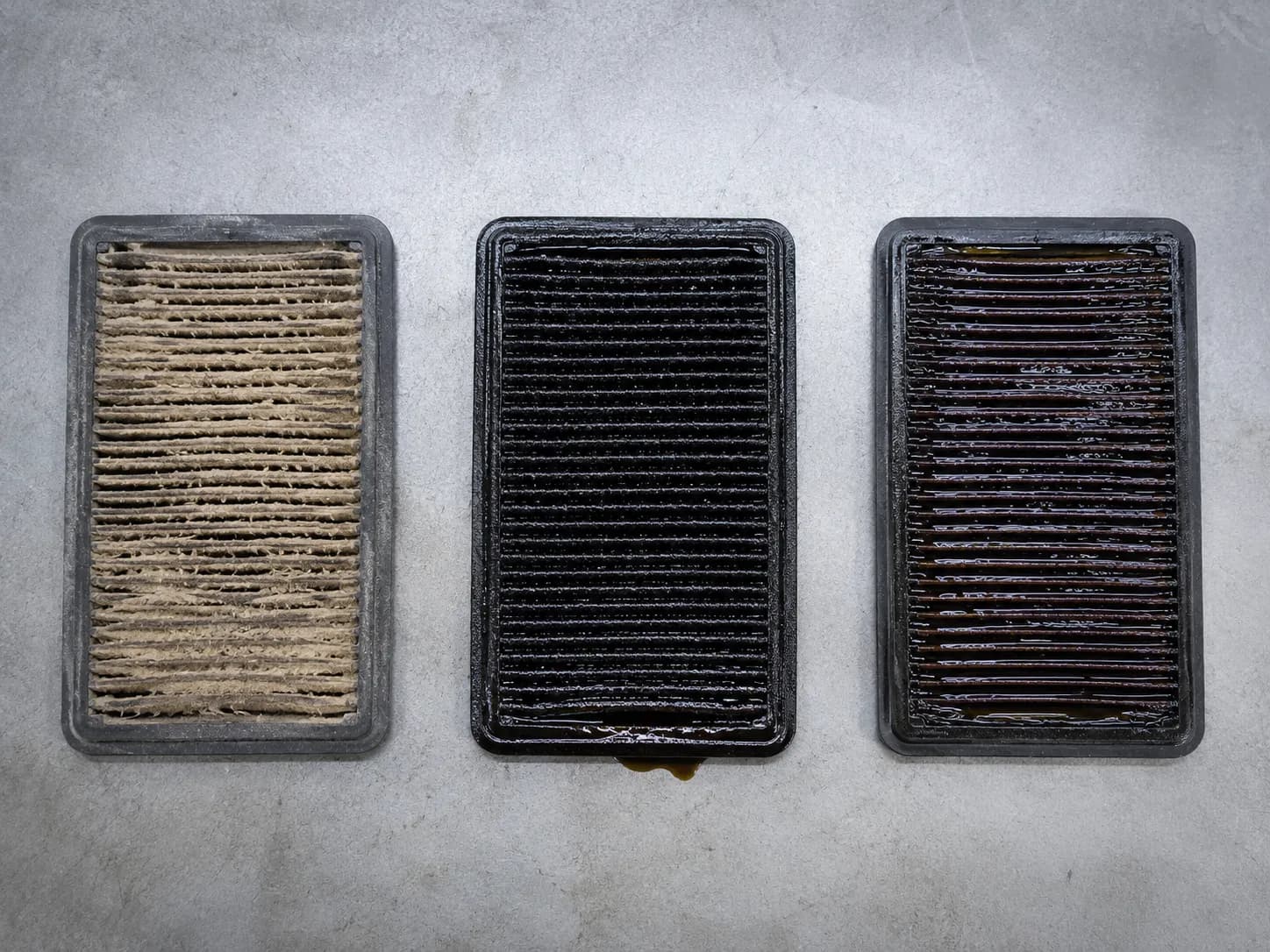 Overhead comparison of three lawn mower air filters showing dust-clogged, oil-soaked, and fuel-soaked elements under identical lighting to highlight contamination differences.