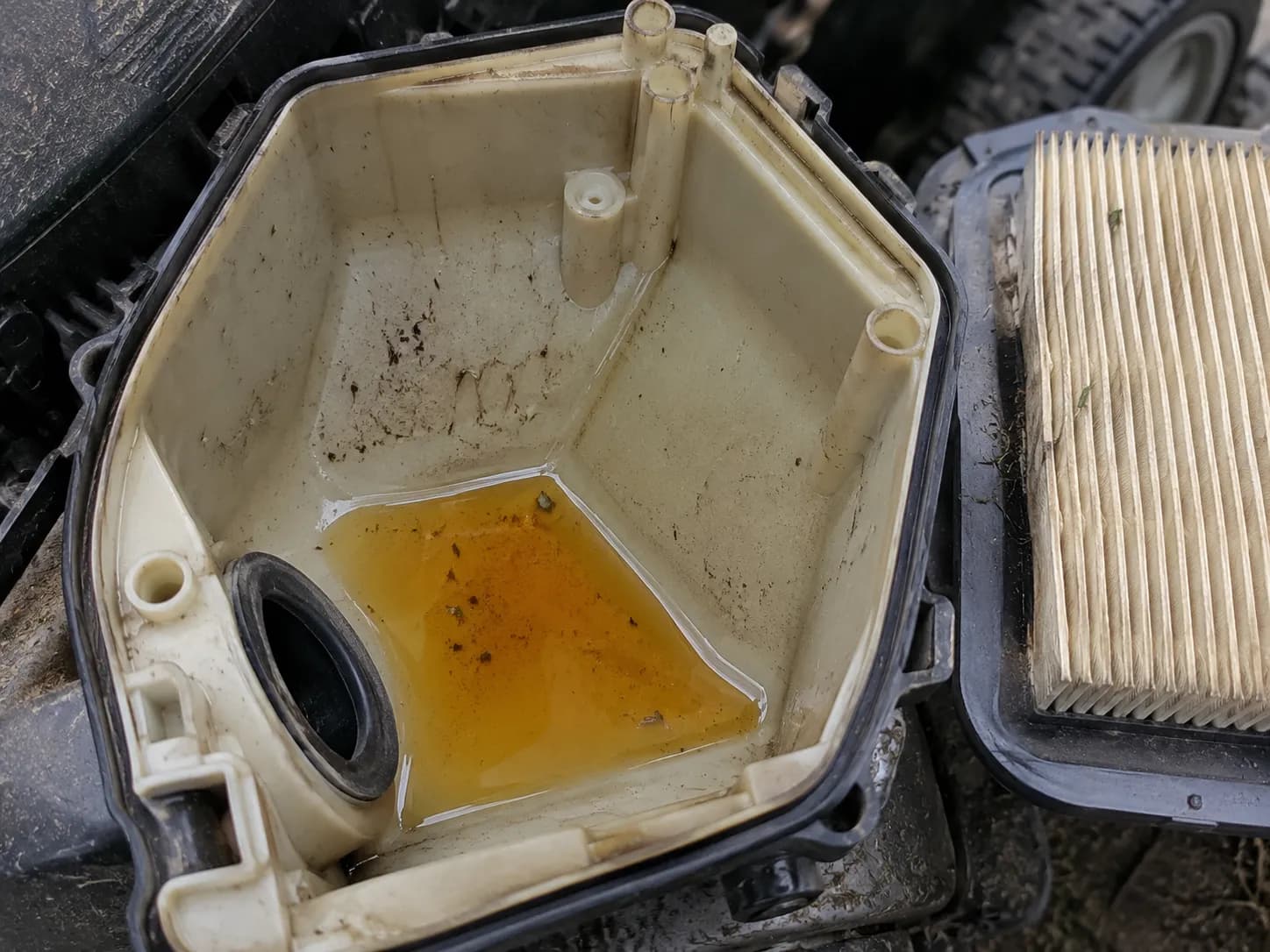 Fuel pooled in the low corner of a walk-behind mower's air filter housing, showing that fuel can remain after the filter itself has dried.