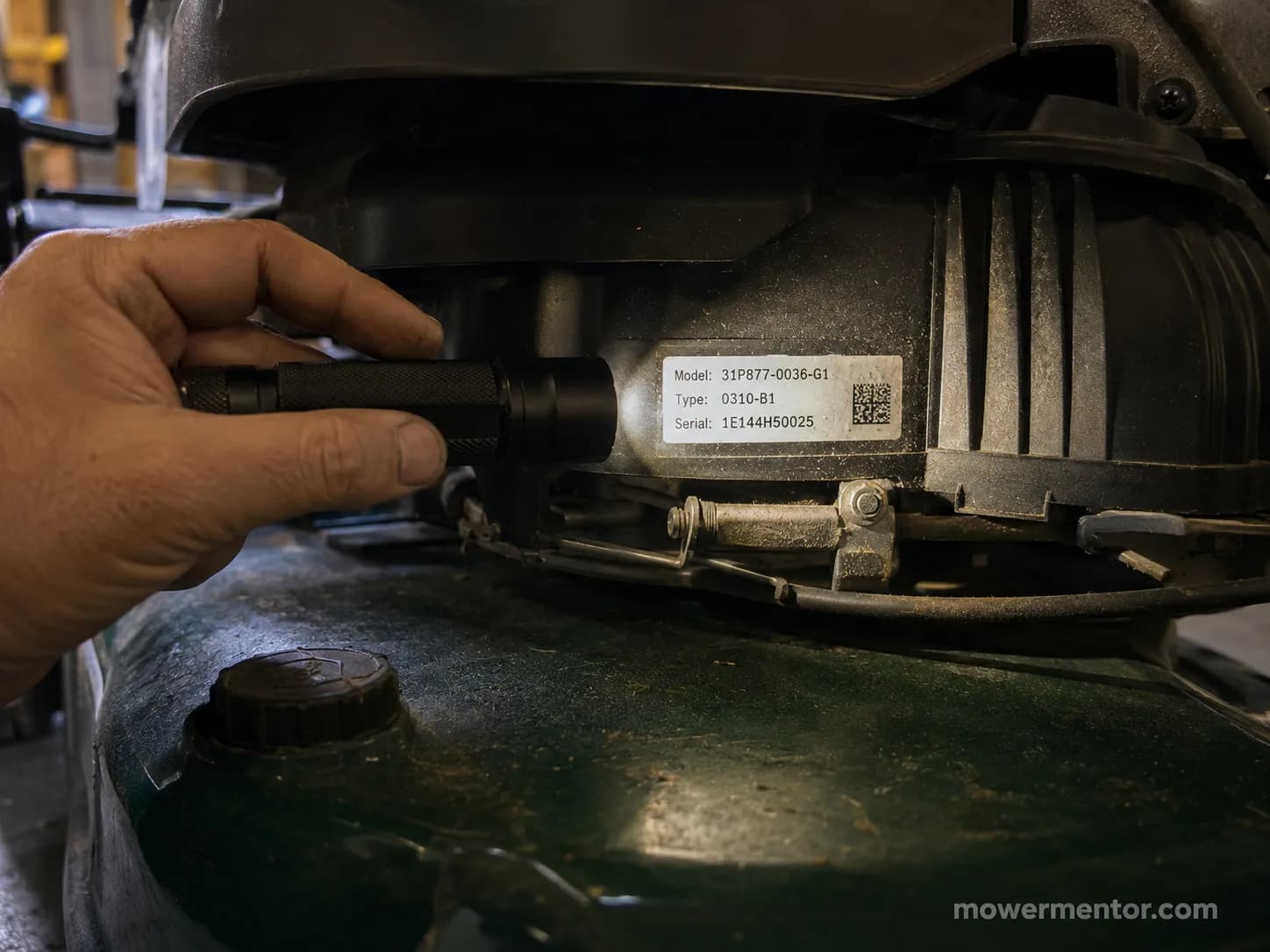 Close-up of a hand using a flashlight to read a lawn mower engine spec sticker showing the model, type and serial numbers.