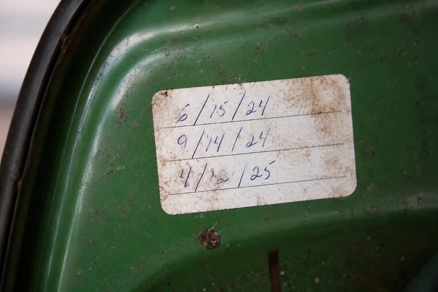 Handwritten lawn mower maintenance log sticker inside a mower deck cover showing three dated tune-up entries with light grease marks.