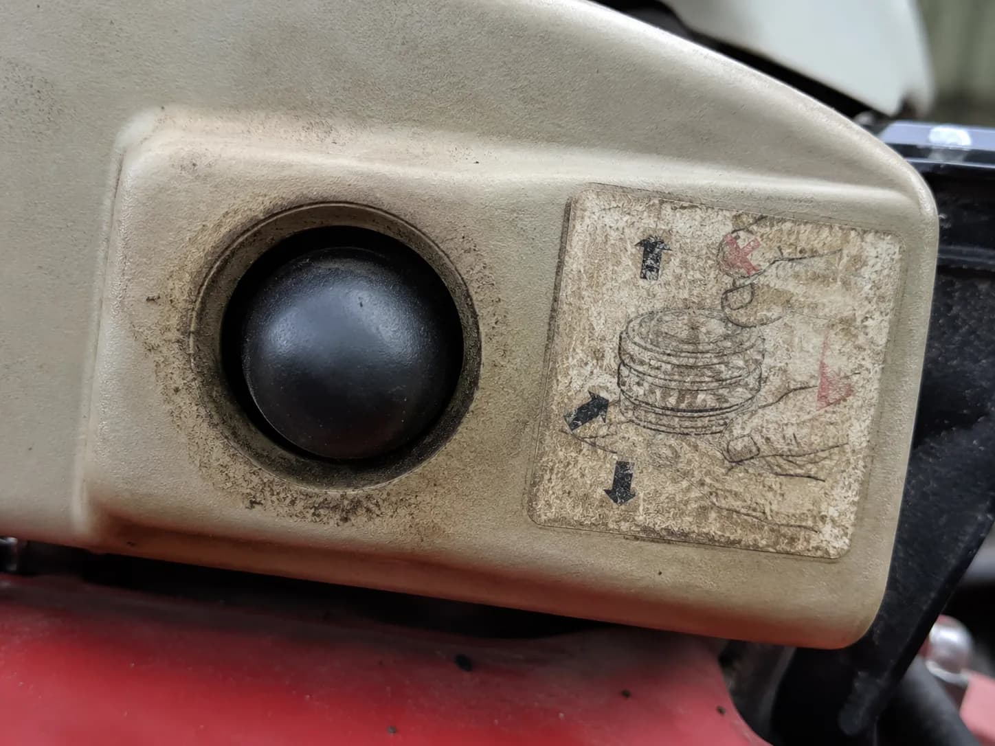 Close-up of a lawn mower primer bulb beside the primer instruction decal on a warm engine, documenting an over-primed condition with roughly a dozen primer presses instead of the recommended three.