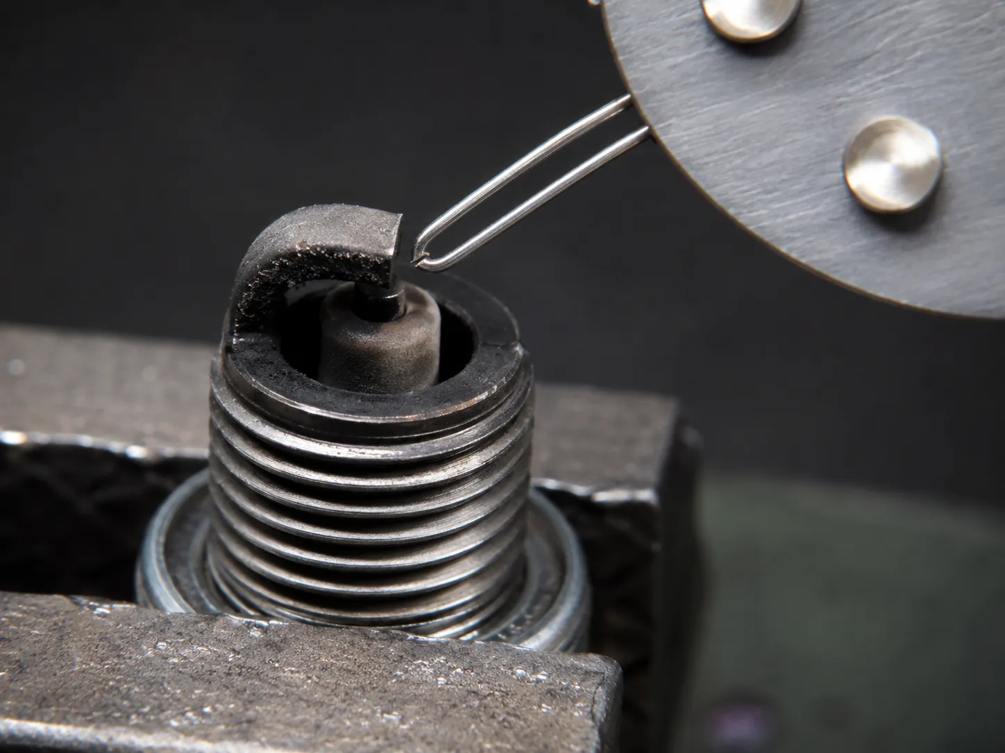 Macro view of a wire-loop spark plug gap gauge checking the electrode gap on a spark plug clamped in a bench vise, showing two adjacent wire loops for accurate small engine spark plug gap measurement.