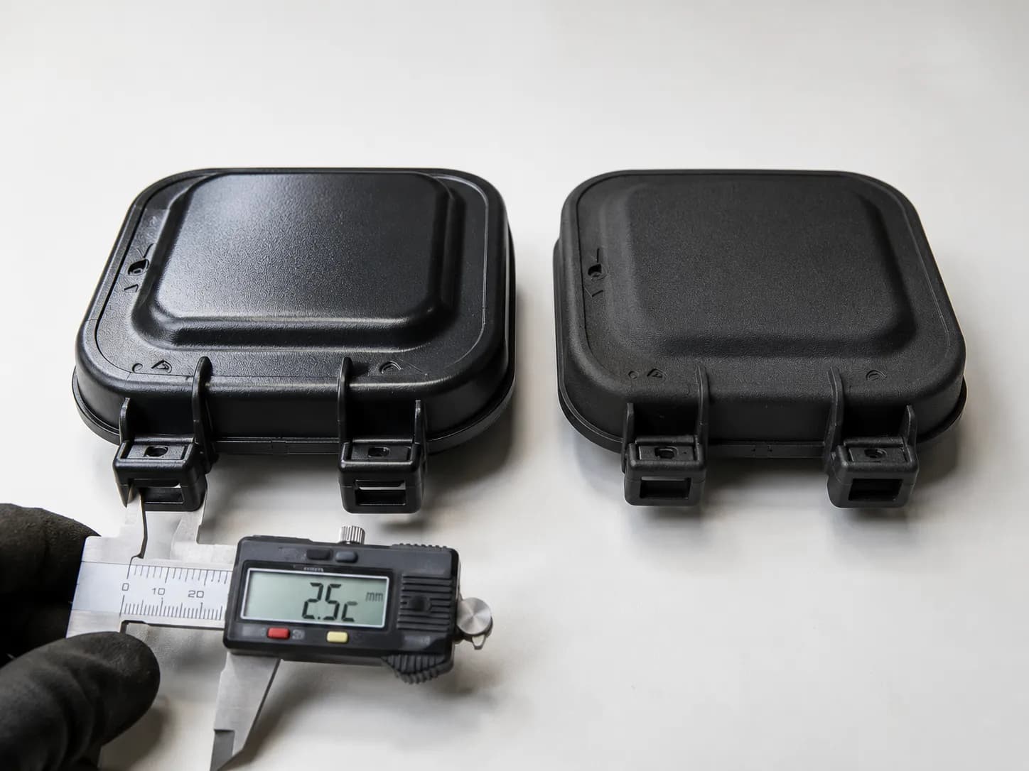 OEM and aftermarket lawn mower air filter covers side by side with a digital caliper measuring latch wall thickness to compare plastic quality and manufacturing differences.