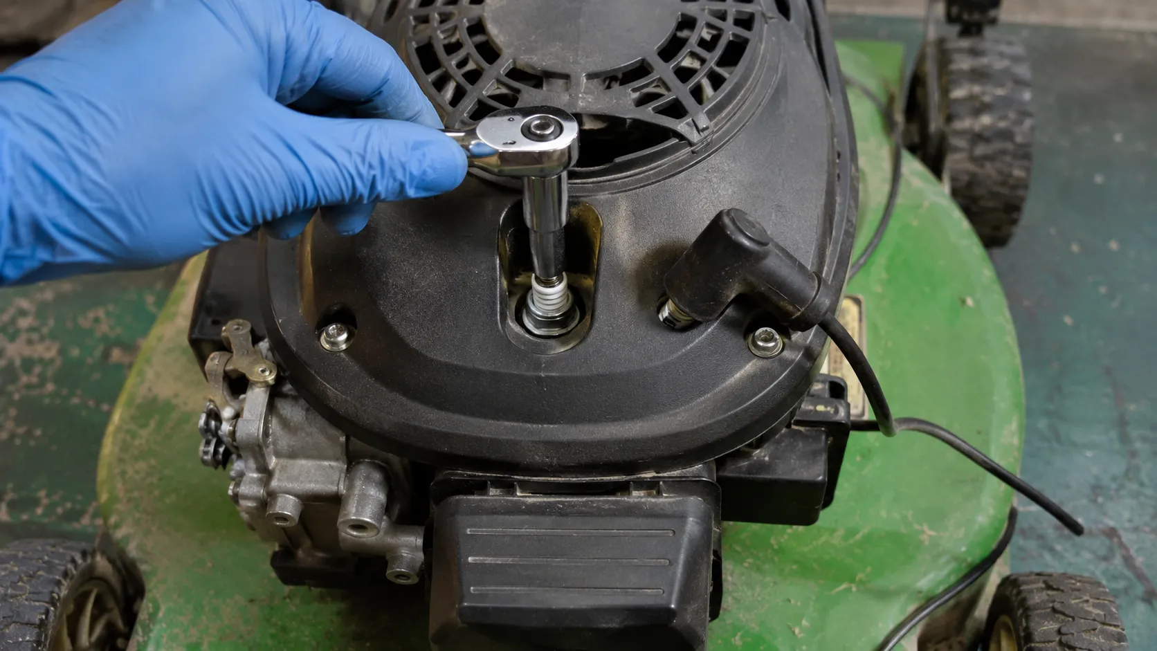 Gloved hand placing a spark plug socket onto the spark plug of an OHV push mower engine with the spark plug boot disconnected and resting to the side before removal.