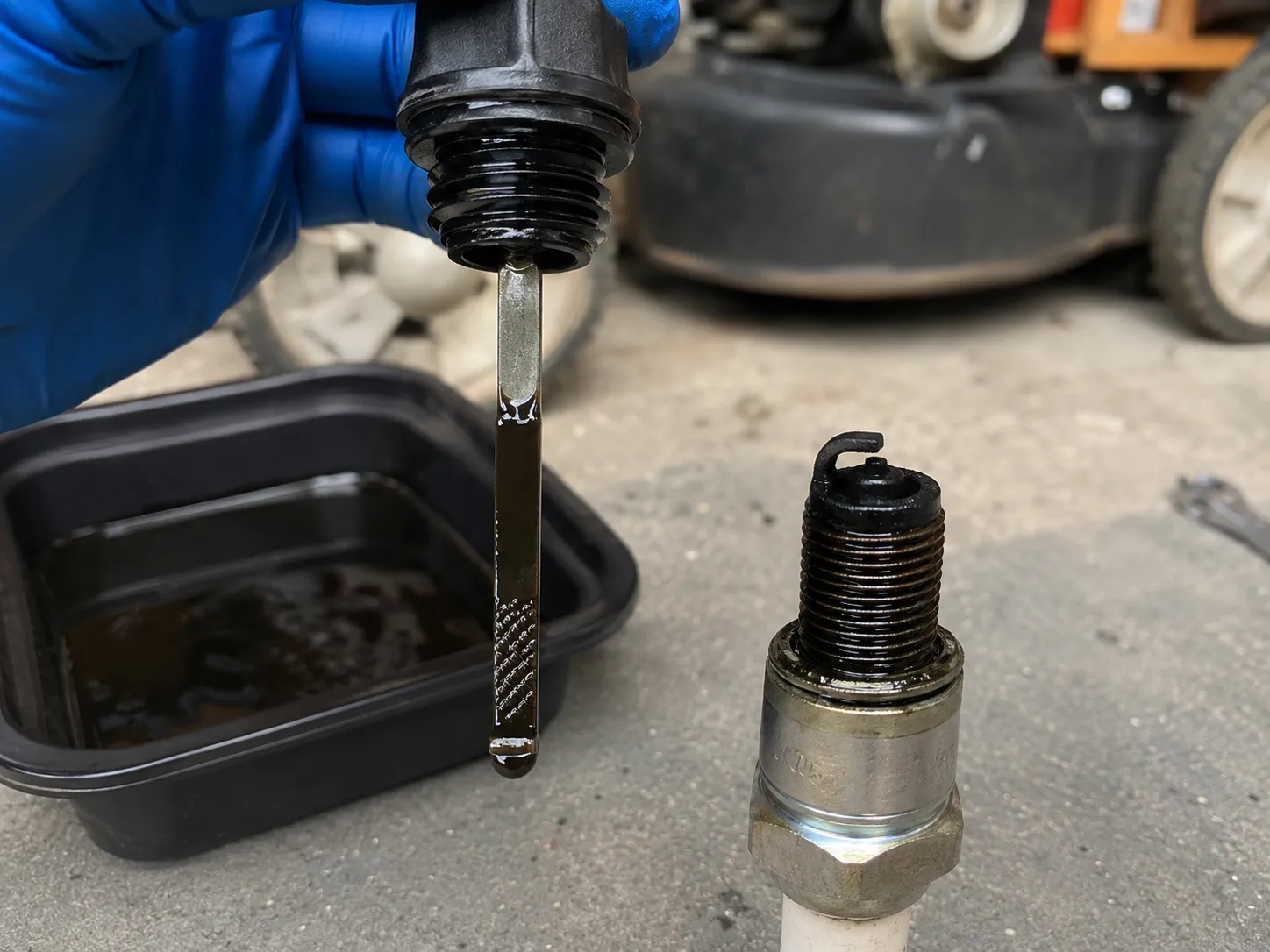 Overfilled lawn mower engine oil dipstick showing the oil level above the full mark beside a wet oil-fouled spark plug after excess oil was drained to the correct level.