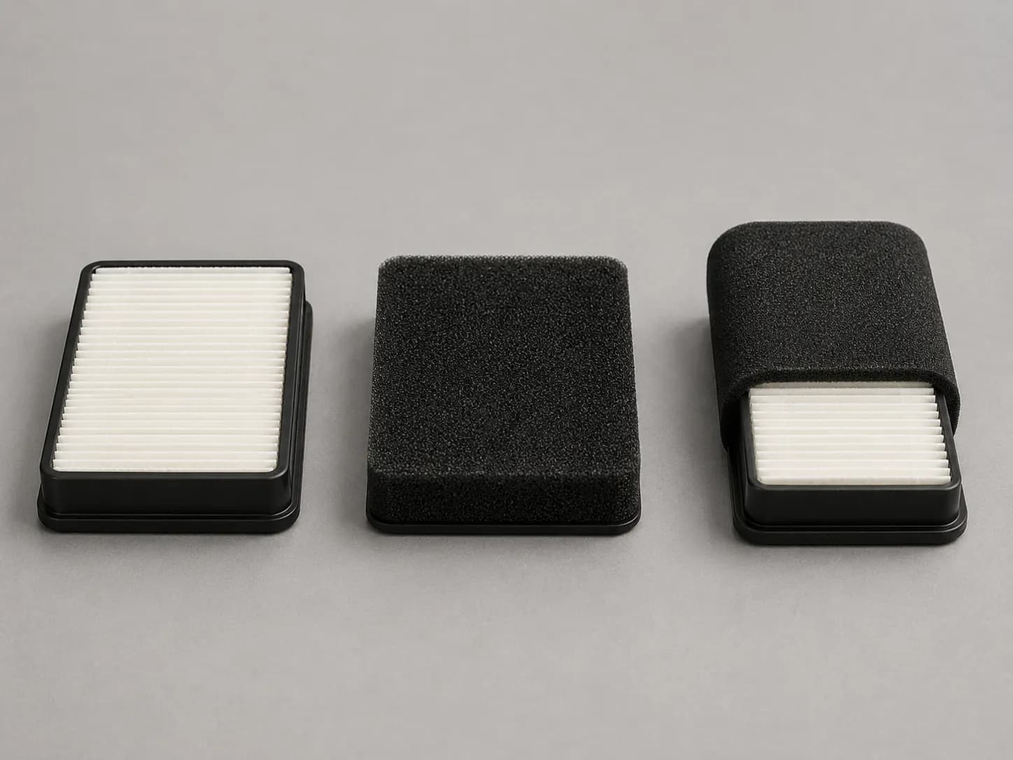 Paper, foam, and dual lawn mower air filters arranged side by side on a light gray surface, showing the differences between pleated paper, foam, and dual-element filter designs.
