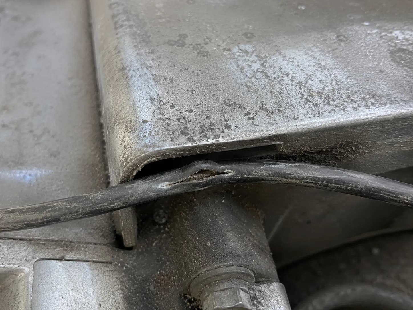 Close-up of a small engine kill wire pinched beneath the blower housing lip, showing flattened insulation with a split caused by improper routing and metal edge compression.