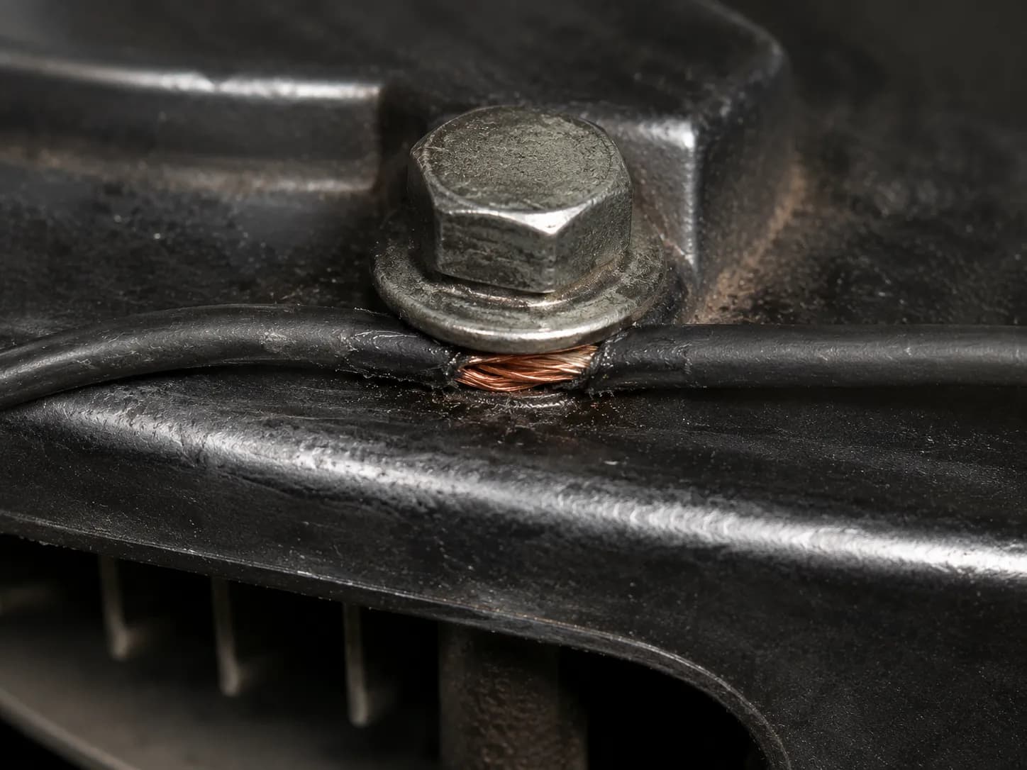 Close-up of a pinched kill wire with insulation worn through beneath an engine shroud bolt, exposing copper strands that can short the ignition circuit.