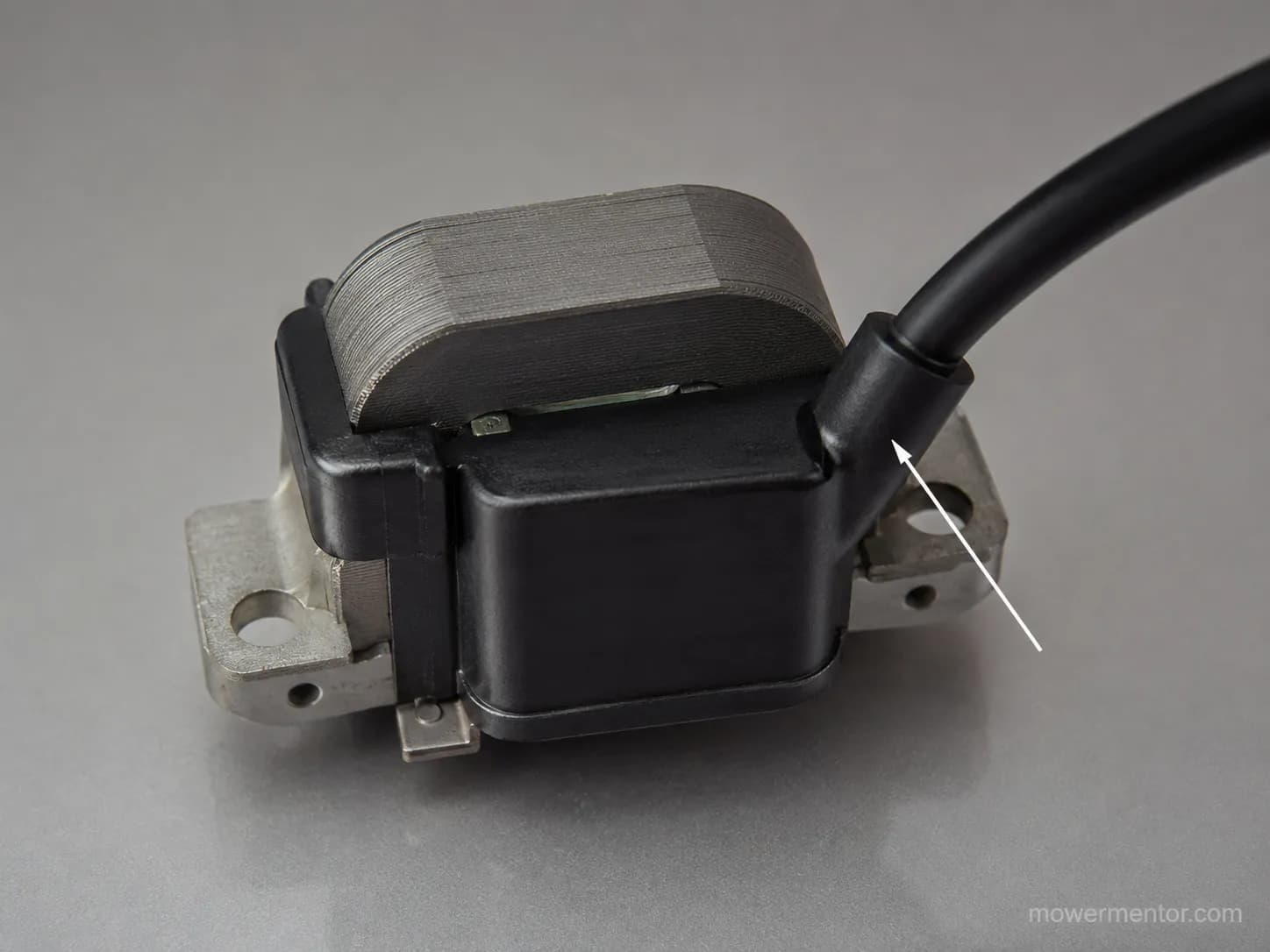 Close-up of a small engine ignition armature with a potted black coil, laminated iron core, high-tension lead, and mounting brackets on a gray surface