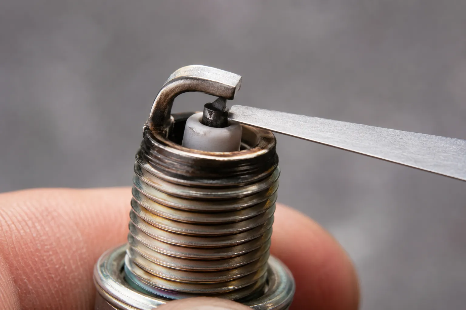 Macro close-up of a feeler gauge set to a 0.030-inch gap between the center and side electrode of a small-engine spark plug.