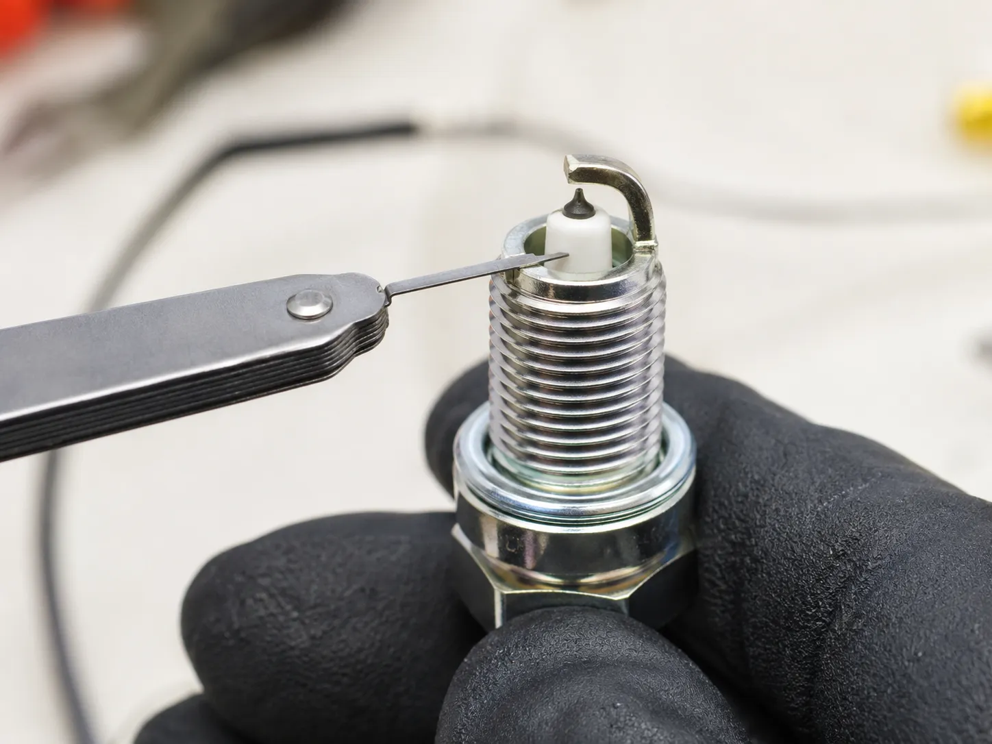 Mechanic uses a wire-style spark plug gap gauge to check the electrode gap on a new spark plug before installation in a lawn mower or small engine for reliable ignition.