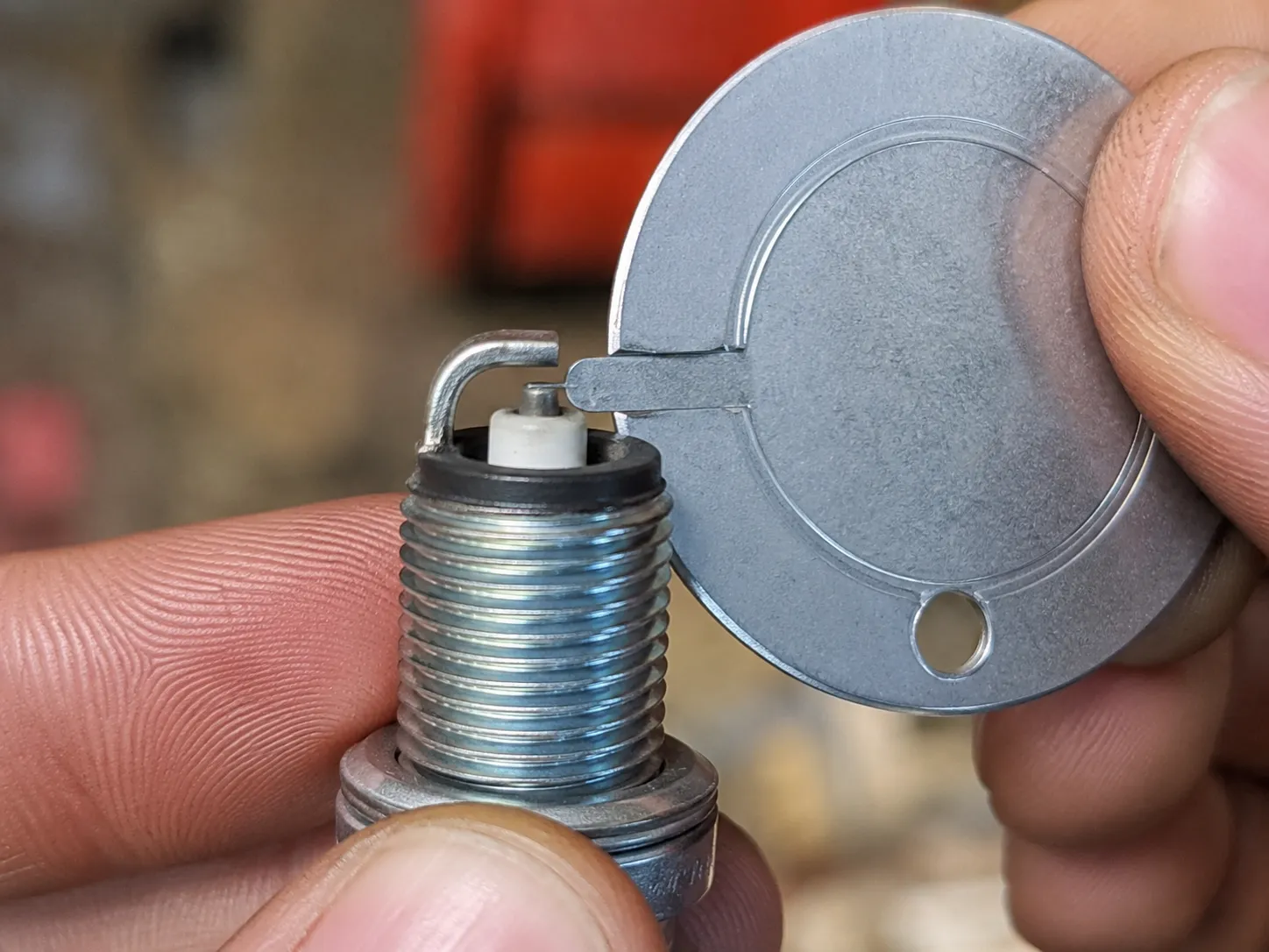 Macro close-up of a coin-style spark plug gap gauge measuring a 0.028-inch electrode gap on an NGK BPMR6A spark plug held between two fingers.