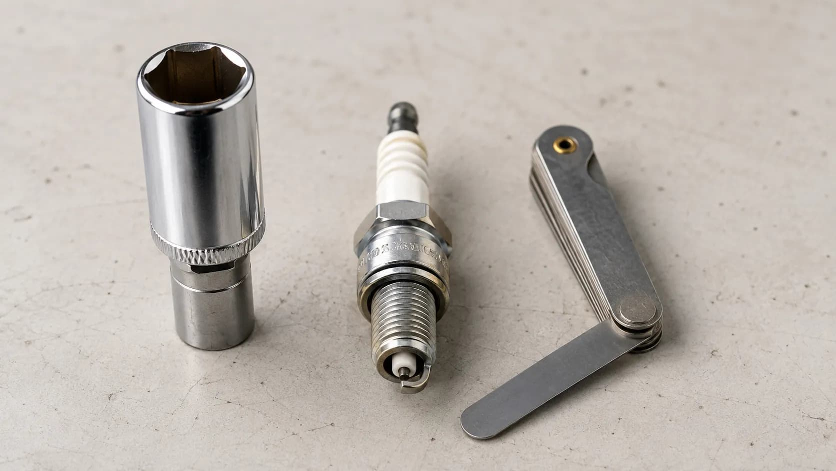 New NGK-style spark plug centered between a 13/16-inch deep socket and a feeler gauge set to 0.030 inch on a clean gray workbench under soft daylight.