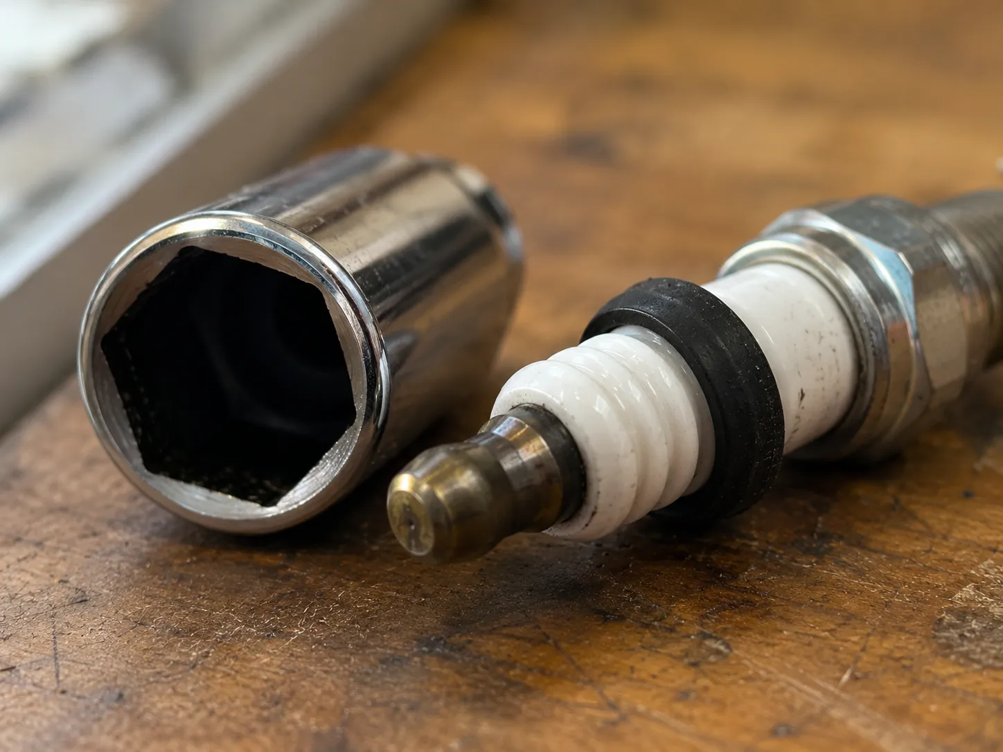 Close-up of a removed spark plug with the rubber retaining grommet still attached to the ceramic insulator beside an empty spark plug socket, illustrating a common socket grommet issue.