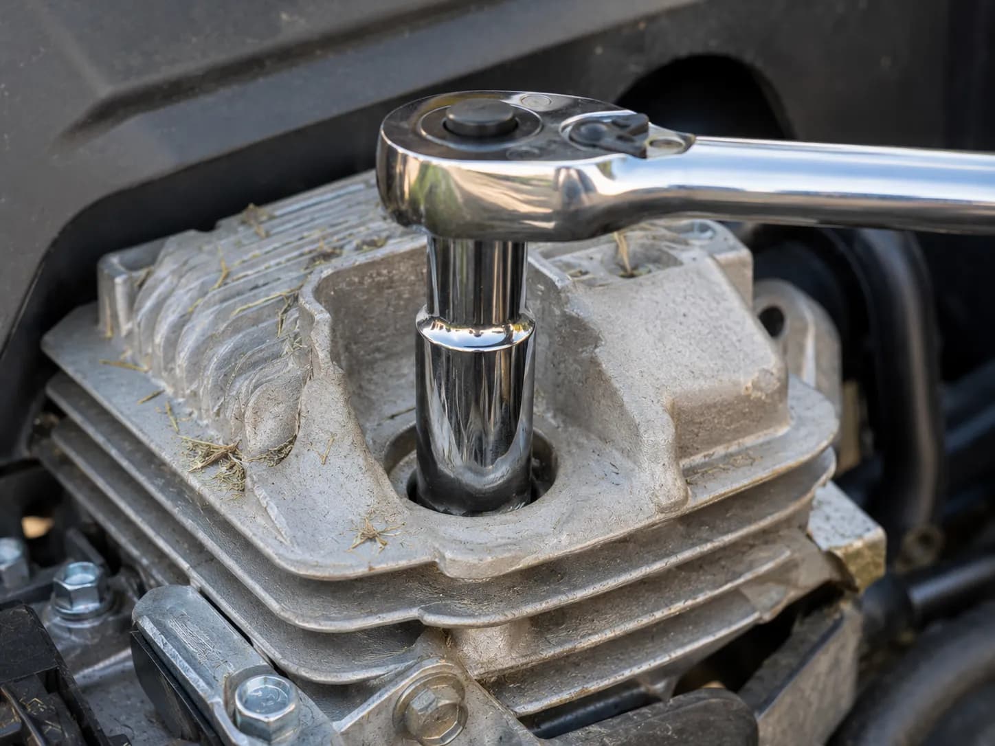 Deep spark plug socket fully seated on a lawn mower spark plug with a ratchet positioned for counter-clockwise removal, showing the correct tool setup before loosening the plug.