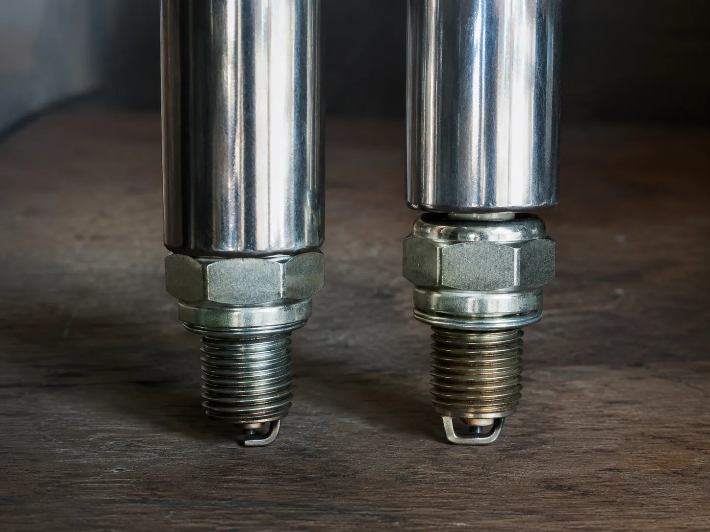 Spark plug socket comparison showing a 5/8-inch hex plug fully seated inside the socket while the socket sits proud on a larger 13/16-inch hex plug on a wooden workbench.