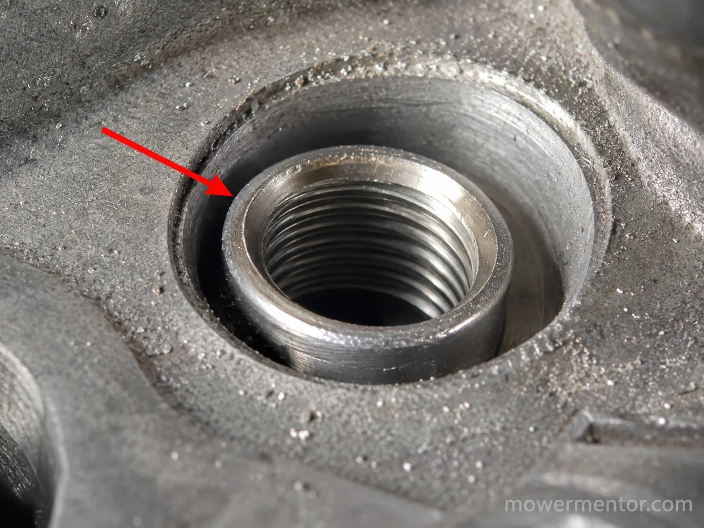 Close-up of a tilted stainless steel threaded insert sitting proud in an aluminium spark plug hole, with a red arrow pointing to the raised edge and aluminium dust around the rim.