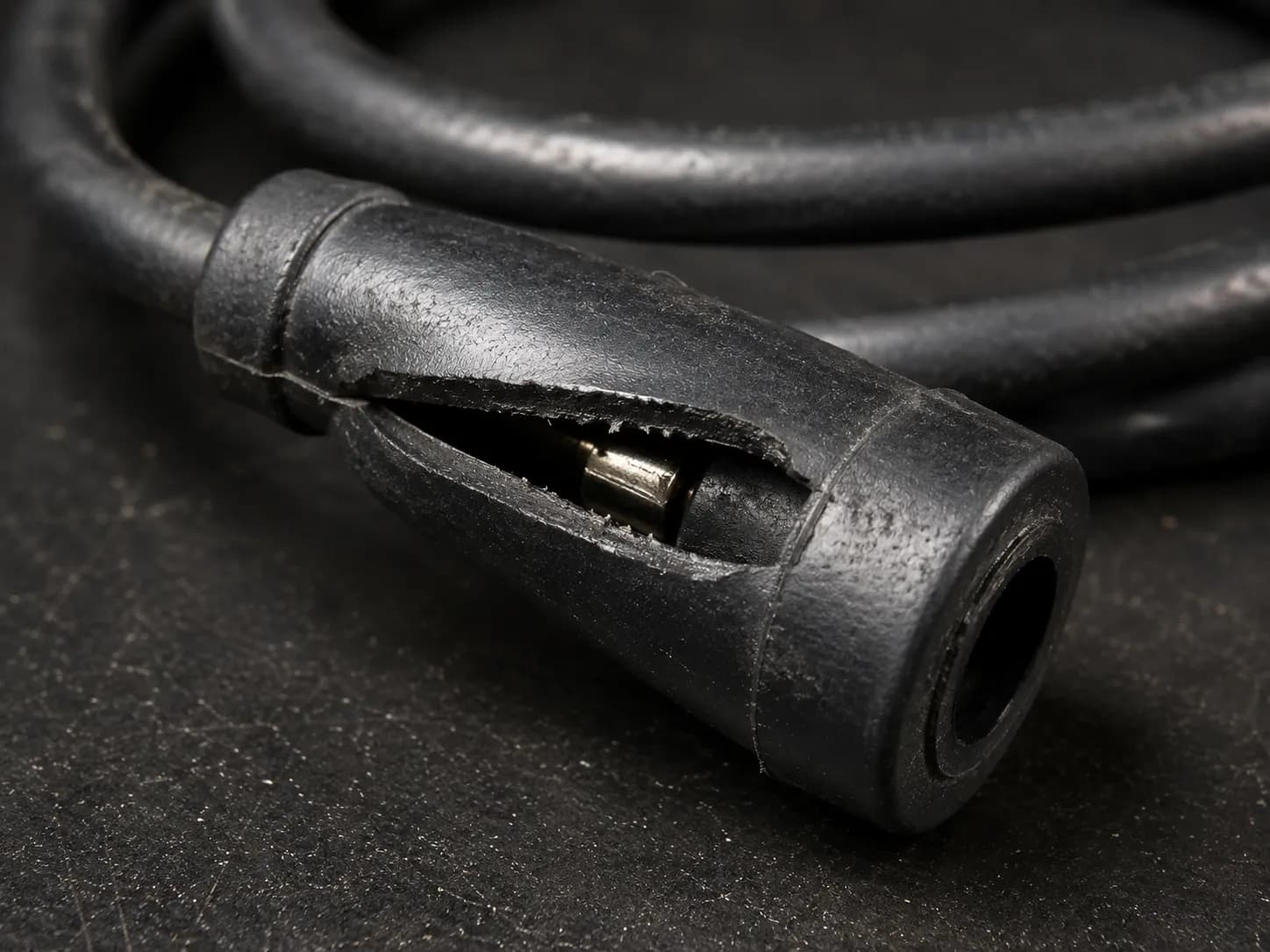 Close-up of a split lawn mower spark plug boot on an ignition lead, revealing the internal metal terminal and damaged rubber that can cause a no-start engine condition.