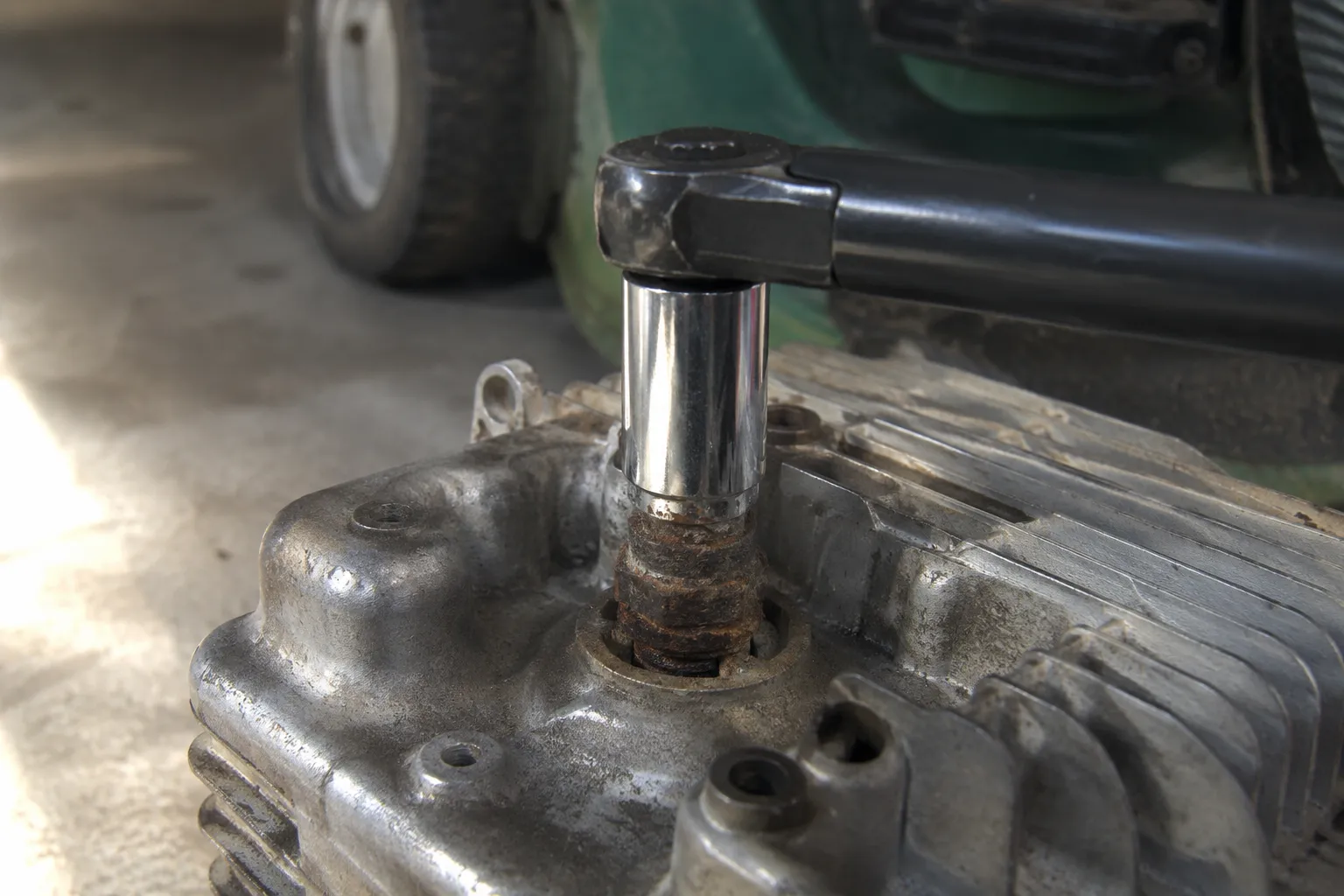 Heavily corroded spark plug seized in a Briggs Quantum aluminum cylinder head with a six-point socket and breaker bar attached, illustrating a stuck spark plug removal attempt.
