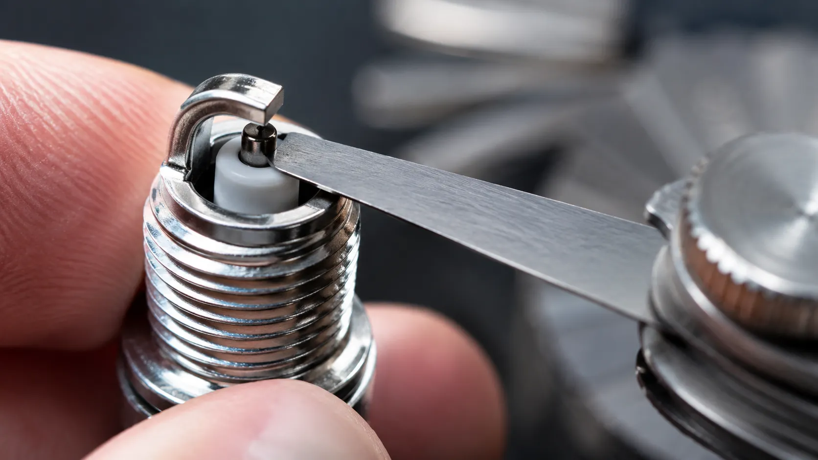 Feeler gauge blade inserted between the center and ground electrodes of a new Toro spark plug to verify the correct gap before installation.