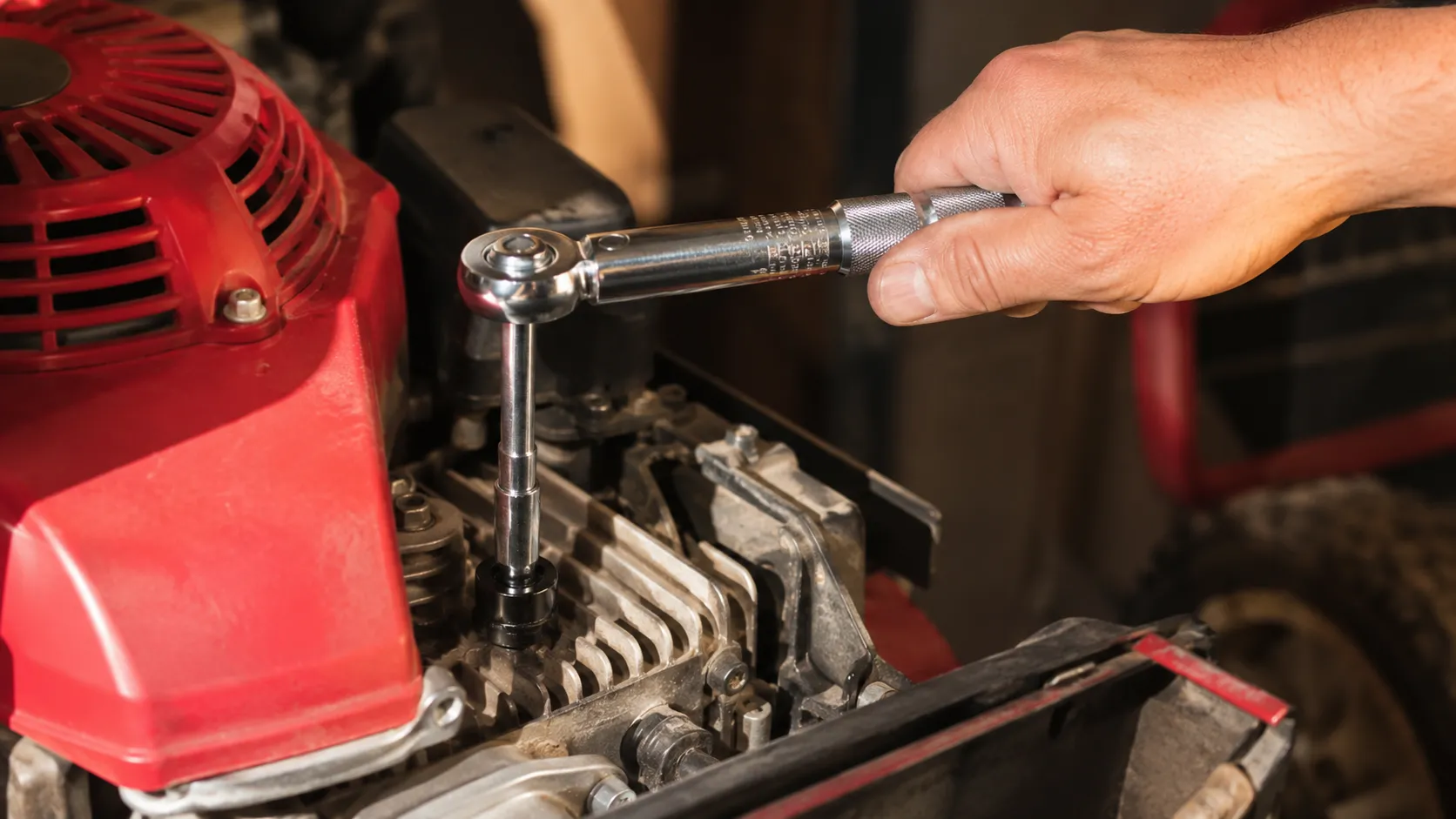 Hand tightening a new spark plug with a small torque wrench on a Honda mower engine, socket aligned straight over the plug during final installation in a well-lit workshop.