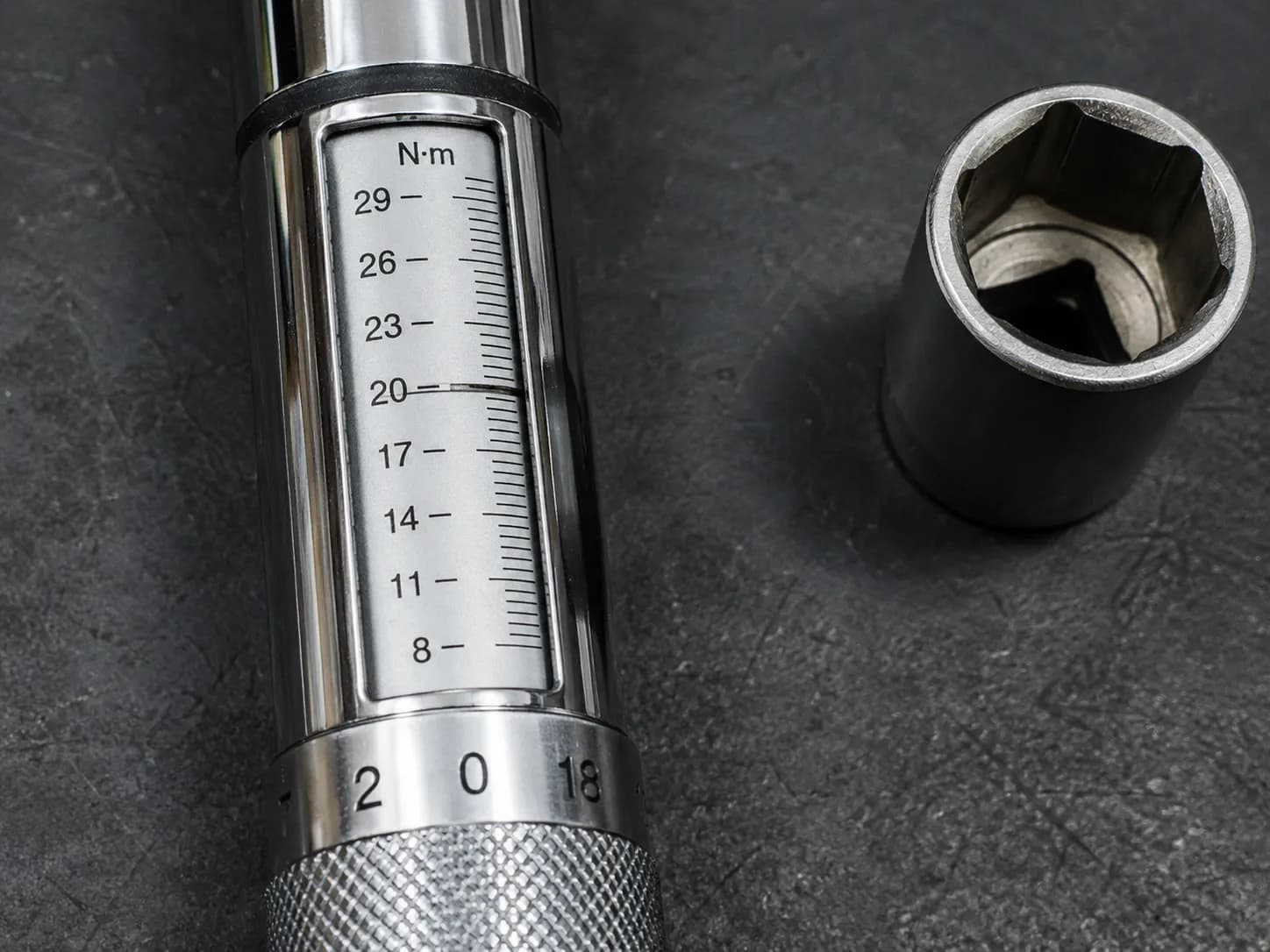Mechanical click-type torque wrench set to 17–20 Nm beside a spark plug socket on a dark workbench, showing the scale window for accurate spark plug tightening and torque adjustment.