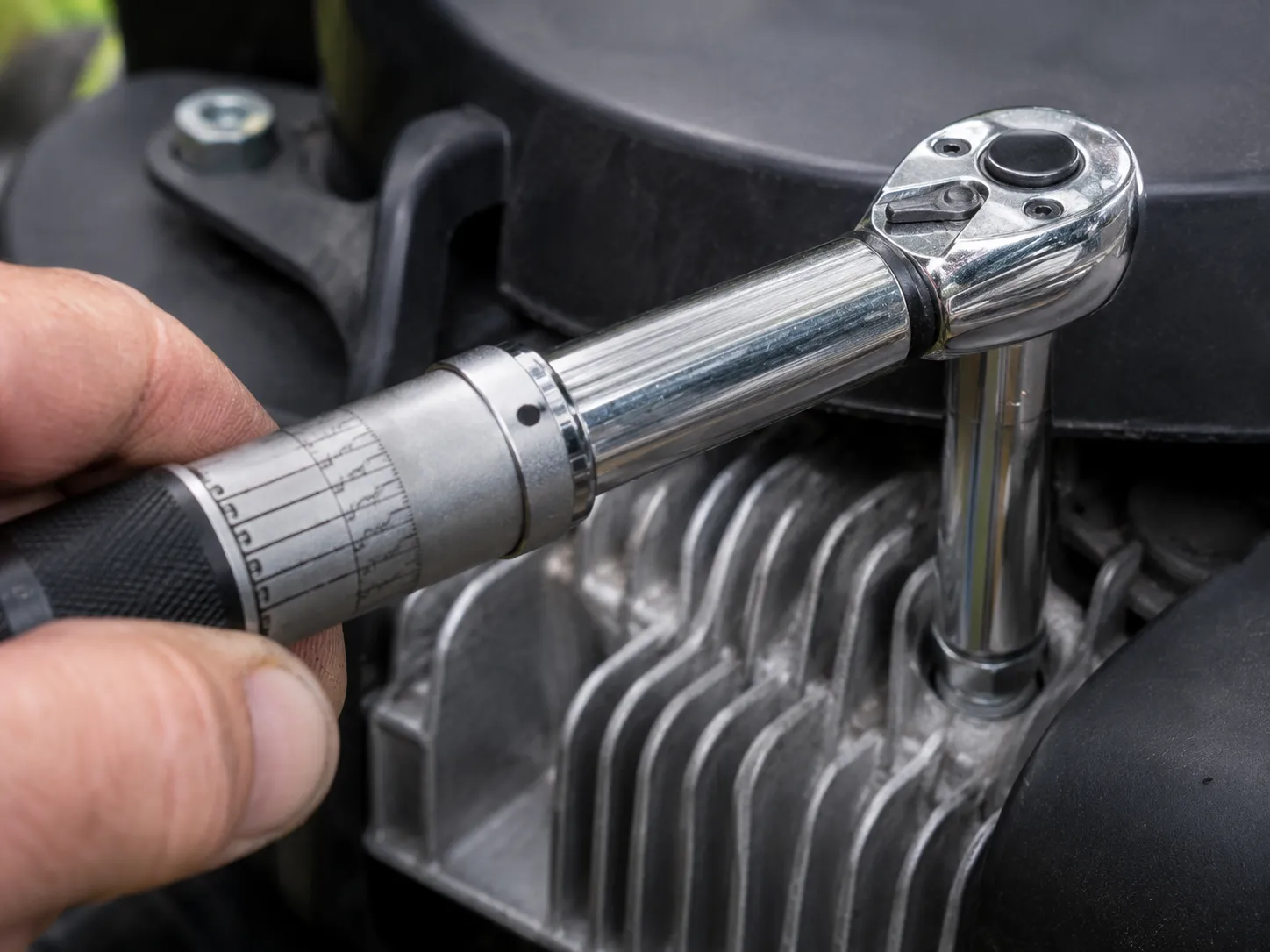 Close-up of a torque wrench tightening a lawn mower spark plug in an aluminum cylinder head, demonstrating proper spark plug installation with controlled torque and a deep socket.